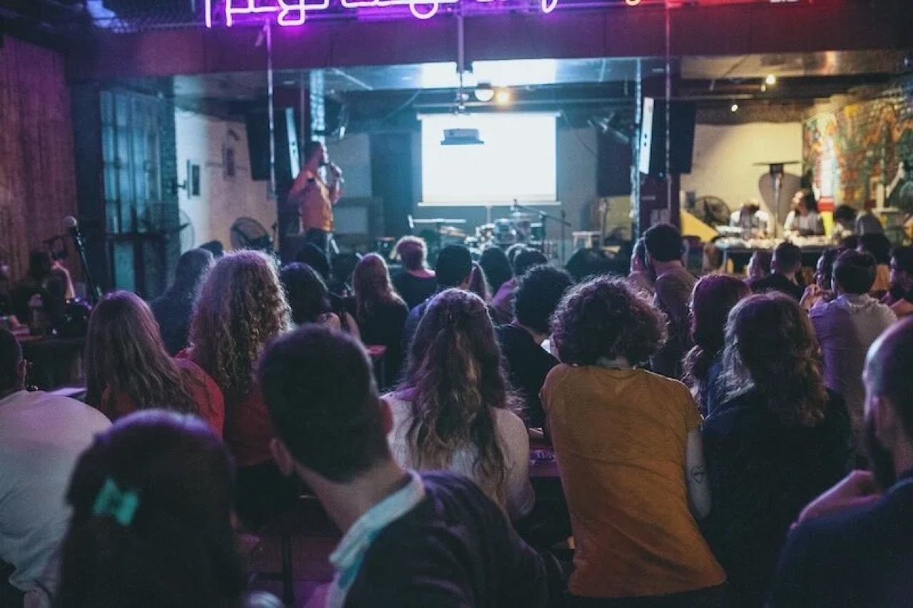 Real Talk Philosophy — audience watching presentation at venue with neon lights